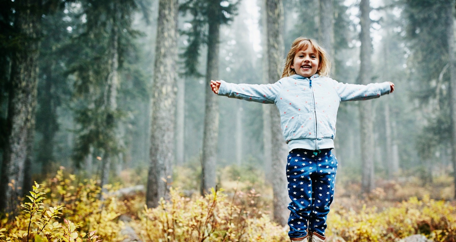 Girl standing with arm outstretched in a forest