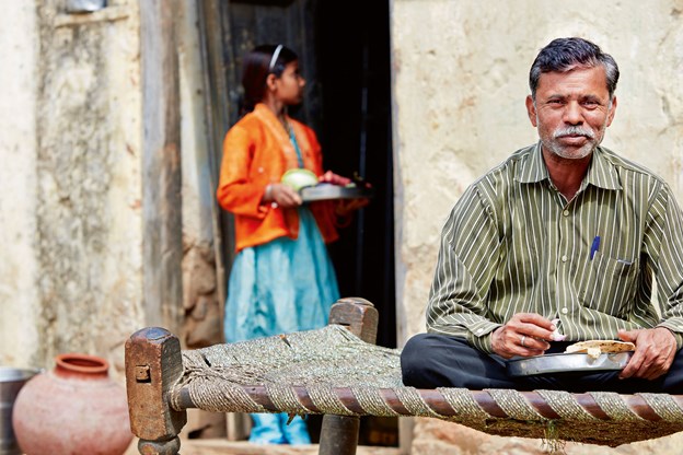 Man sitting cross-legged on cot with woman in background