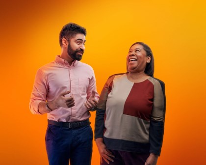 Two people laughing together against an orange background