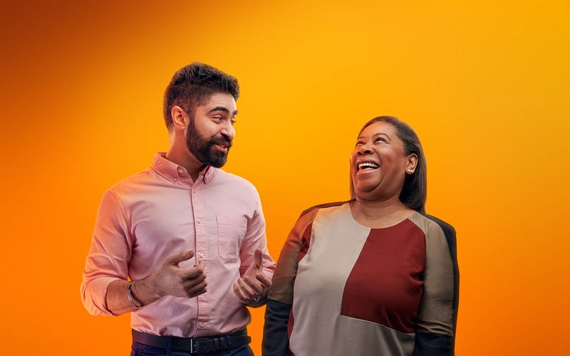 Two people laughing together against an orange background