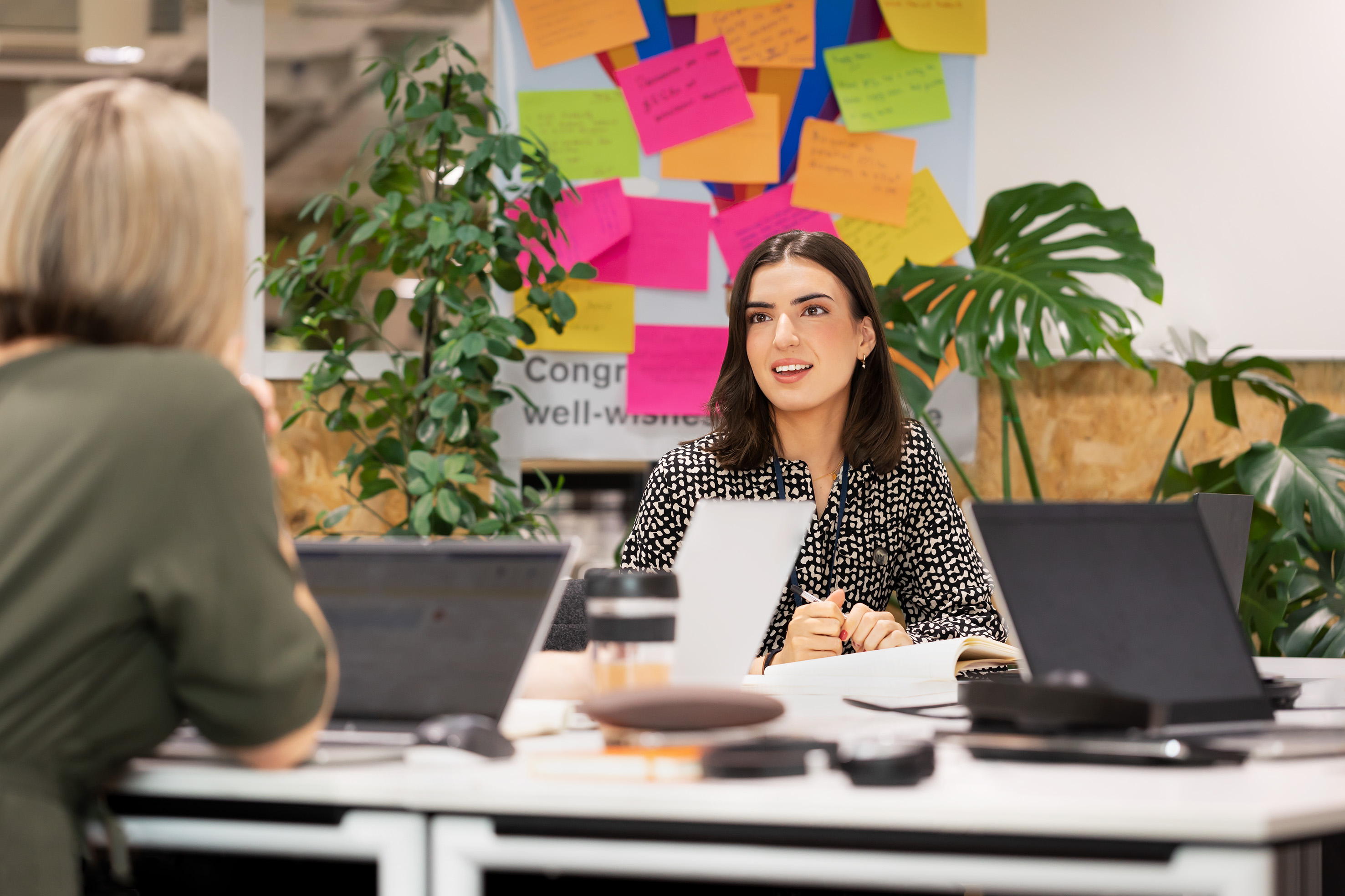 Two women speaking together over a desk in an office.