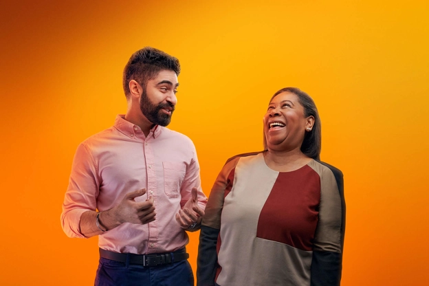 Two people laughing together against an orange background