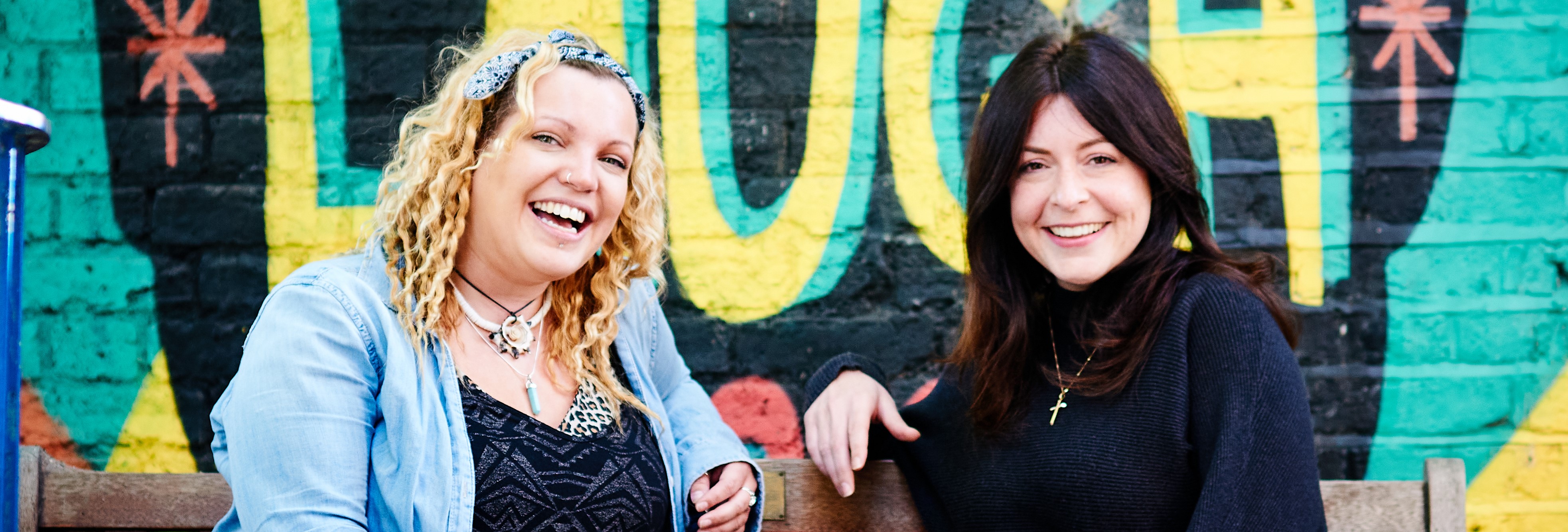 Two Women Laughing in Front of a Laugh Mural
