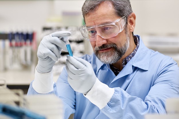 Man in laboratory setting inspecting a blue vial