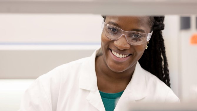 Woman in labratory coat and safety glasses smiling